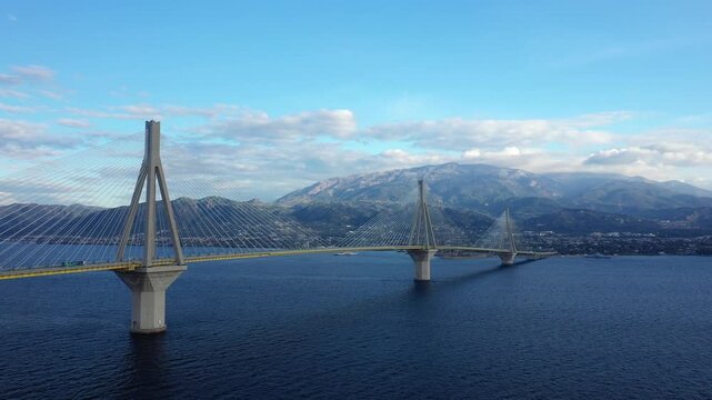 Wide view of the Rion Antirion Bridge spanning across deep blue water with mountains in the background, Patras, Greece.