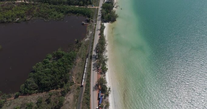 Top-down aerial fuel tanker train on tracks parallel to a coastal road and sandy beach