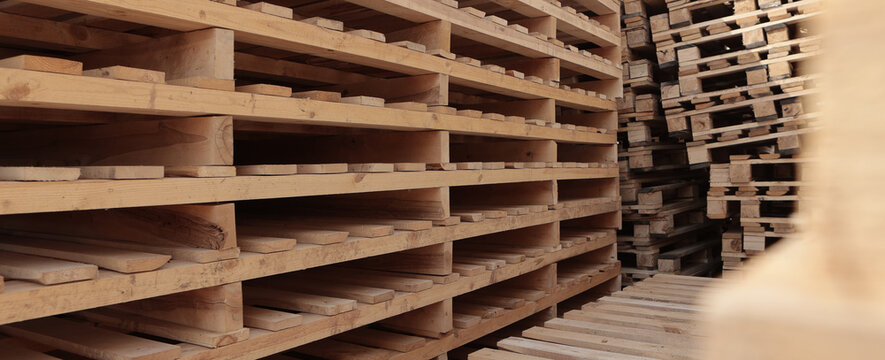 Stacks of wooden pallets for heavy cargo transportation. Lumber warehouse in the open air. Wooden pallets. A narrow banner.