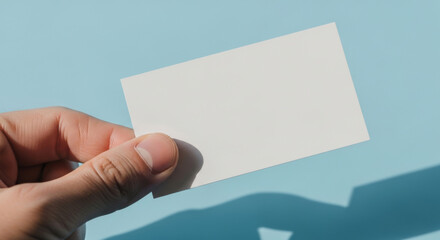 Obraz premium Close-up of a Hand Holding a Blank White Card Against a Soft Blue Background, Symbolizing Opportunities and Creativity