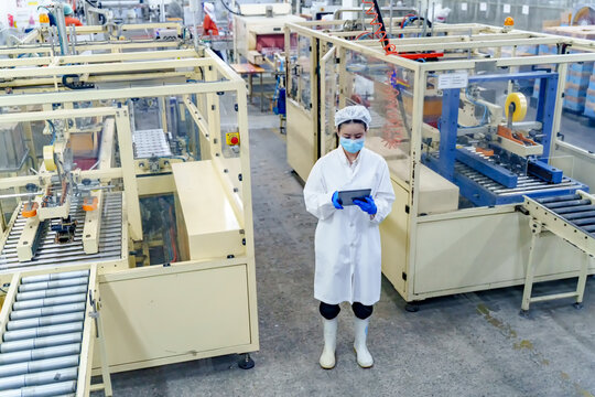 Factory worker in protective gear uses tablet to monitor automated production line machinery