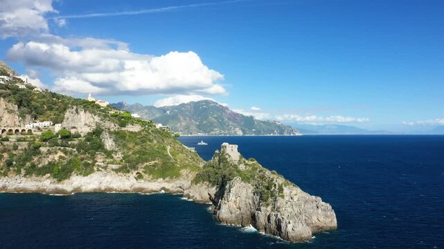 Aerial view of the dramatic Capo di Conca coastline with a historic watchtower overlooking the blue sea on the Amalfi Coast, Italy. Lush green hills and rugged cliffs meet the Mediterranean under a