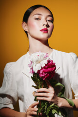 Young fashionable woman with flawless makeup and red lips holds fresh flowers against a bright...