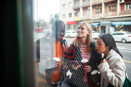 Friends window shopping with coffee on city street