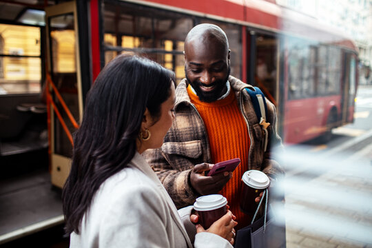 Smiling friends with coffee using smartphone at city bus stop