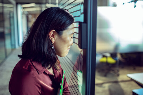 Stressed businesswoman leaning on glass wall in modern office hallway