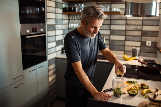 Middle-aged man squeezing lemon into smoothie in home kitchen