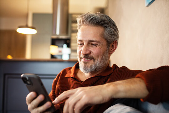 Smiling middle-aged man using smartphone at home