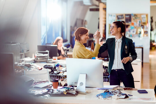 Happy female coworkers high fiving in creative fashion design office