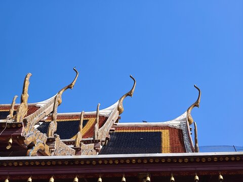Golden Chofa Ornaments on Thai Temple Roof Against Blue Sky