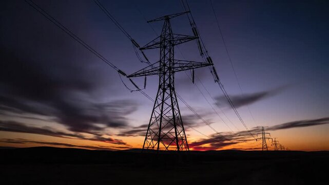 Silhouette of high voltage power lines and transmission towers against a vibrant sunset sky.
