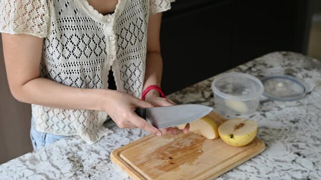 Calm asian woman embraces healthy home lifestyle focused on wellbeing. Finding moments to relax in kitchen, cutting fresh pear for simple nutritious snack