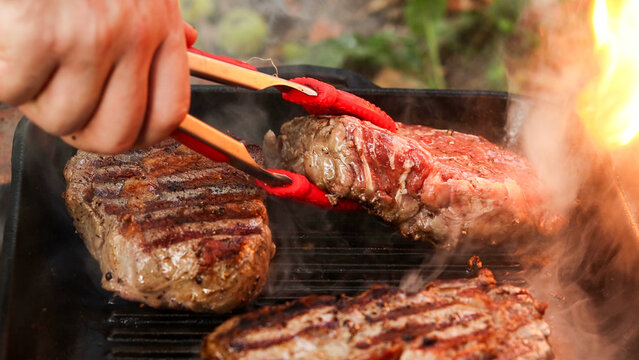 Juicy beef steaks sizzling on a cast iron grill pan with flames licking the side