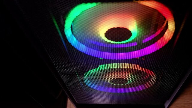 Close up shows RGB ring lights glowing inside a gaming PC case, colorful fans behind a mesh panel in the dark. Neon aesthetics drive PC culture, but efficient cooling and power use still matter.