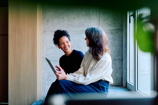 Two diverse business women collaborating and discussing content on a digital tablet, fostering mentorship and connection in an office