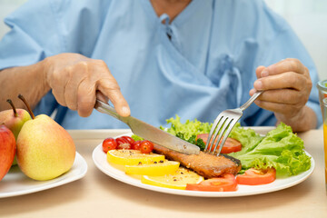 Asian elderly woman patient eating salmon stake and vegetable salad for healthy food in hospital.