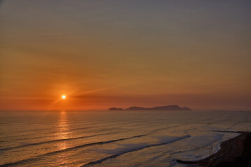 Obraz premium Golden sunset over the Pacific Ocean viewed from the Malecón in Miraflores, Lima, with San Lorenzo Island on the horizon. Scenic coastal landscape promoting active lifestyle, wellness