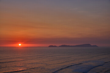 Obraz premium Golden sunset over the Pacific Ocean viewed from the Malecón in Miraflores, Lima, with San Lorenzo Island on the horizon. Scenic coastal landscape promoting active lifestyle, wellness