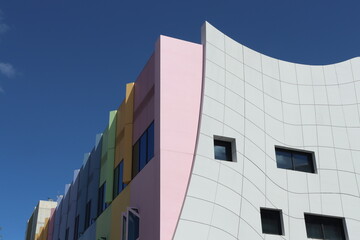 Modern architectural facade featuring white curved design with vibrant rainbow colors and geometric windows against a blue sky