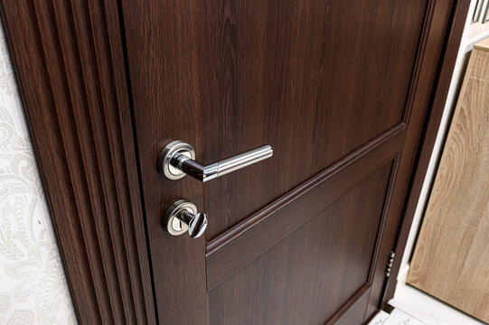 dark brown wooden interior door with a modern metallic lever handle and a round twist lock, sleek design, smooth finish, elegant and functional.