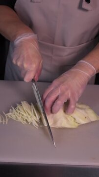 The cook's hands are cutting cabbage in close-up