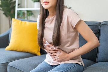 Obraz premium Sick asian young woman in pain, hand holding belly, stomach pain from food poisoning, girl hurt abdomen ache and digestive problem, gastritis or diarrhea. Health care inflammation, abdominal problem