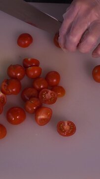 The cook is slicing red cherry tomatoes for the salad. We prepare healthy food and homemade meals