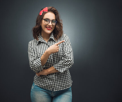 Presentation. Woman pointing to blank space - copy space, girl presenting your product over dark gray - black background. Promoter shows space for your text.