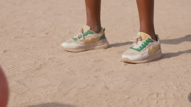 Dirt pitch closeup of sneakers, aspiring striker poised to kick, worn greenandwhite trainers, pink ball edging into frame, warm sunlight and dusty ground texture, slowmotion focus on footwork