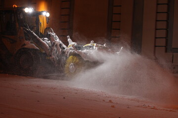 A tractor with a brush clears the road from snow. Repair, cleaning of roads in winter. City improvement services in the cold season. A snowplow cleans the sidewalks. A snowplow clears streets of snow. © Dmitry Presnyakov