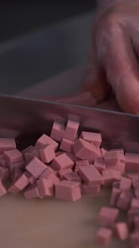 The cook cuts the sausage for the salad. Preparation of appetizers and salads