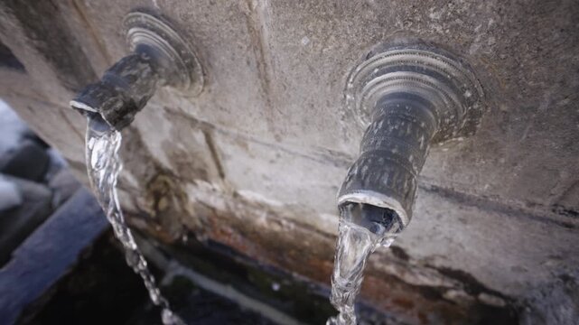 Vintage bronze pipe faucets on the public street with drinkable water flowing in slow motion