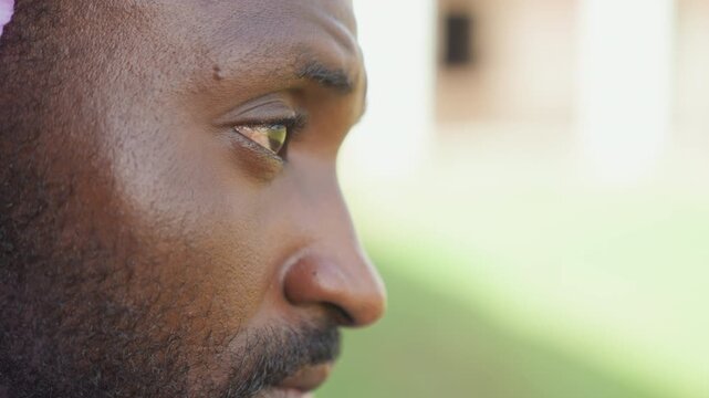 Male athlete profile closeup outdoors intense gaze bearded man side view sweating after training sunlight on textured skin blurred green background runner taking recovery pause thoughtful expression