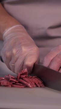 The cook cuts the sausage for the salad. Preparation of appetizers and salads