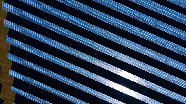 Close up top down view of photovoltaic panels grid. Abstract geometric pattern of blue solar cells with bright sun glint reflection.