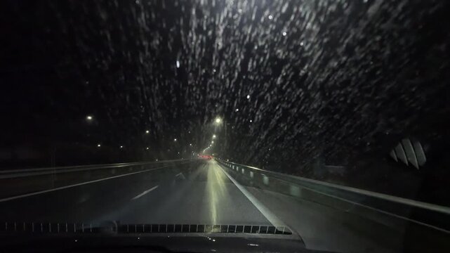 Night driving in rain on two-lane road with raindrops on windshield