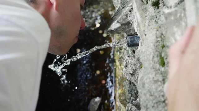 Thirsty hiker person drink pure water from mountain forest pipe tap from cold stream, slow motion