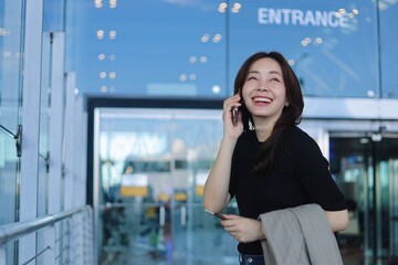 Fototapeta premium Smiling young Asian woman holding passport inside modern airport terminal. Concept of international travel, business trip, relocation.