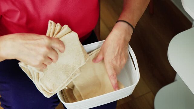 A person sits at a table organizing and folding clean cloths into a basket.