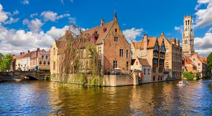 Naklejka premium Bruges, Belgium. Ancient medieval european city. View tower Belfort van Brugge vintage building bank Rozenhoedkaai channel river. Panoramic view blue sky clouds. Famous tourist attraction.