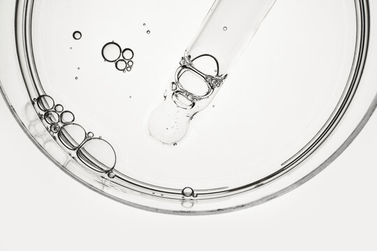 Pipette dropping clear liquid into glass petri dish, creating small bubbles