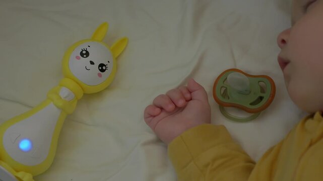 caucasian baby sleeping beside glowing toy and pacifier, dreaming sleeper in yellow onesie on soft pillow with gentle nightlight glow, serene nap routine, tranquil nursery ambiance