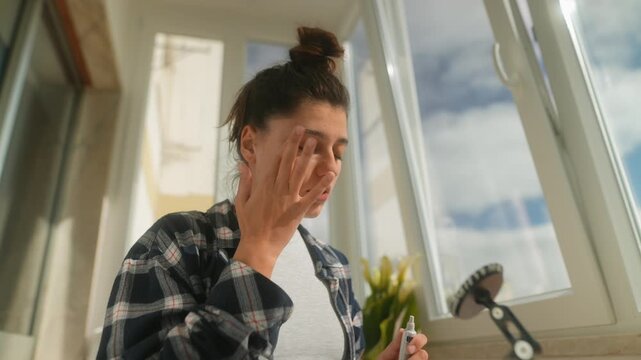 Casual woman gently applying drops before virtual meeting