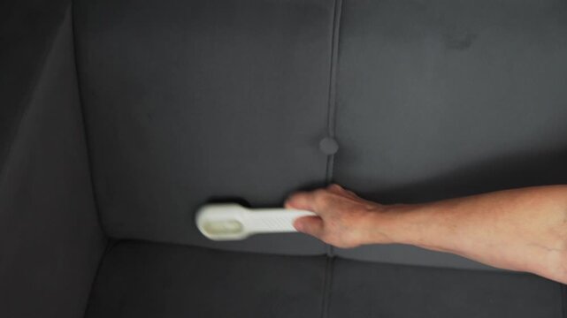 A person is using a brush to clean the surface of a gray chair.