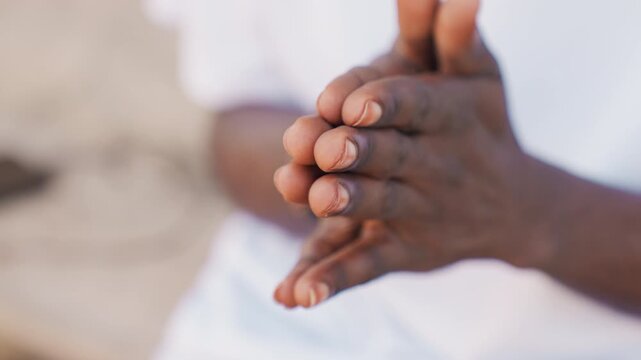 Black athlete hands warming before workout, darkskinned male rubbing palms together on sandy bench, white shirt visible, closeup detail of fingers and knuckles, quiet focused preparation for training