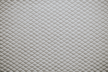 Fototapeta premium Surface of a quilted fabric showing a repeated diamond pattern in a neutral tone for use as background or texture