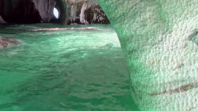 Explore the shimmering grottoes of the Marble Caves in Patagonia. Sunbeams dance on vivid emerald waters, illuminating the beautifully sculpted geological formations within this natural sanctuary.