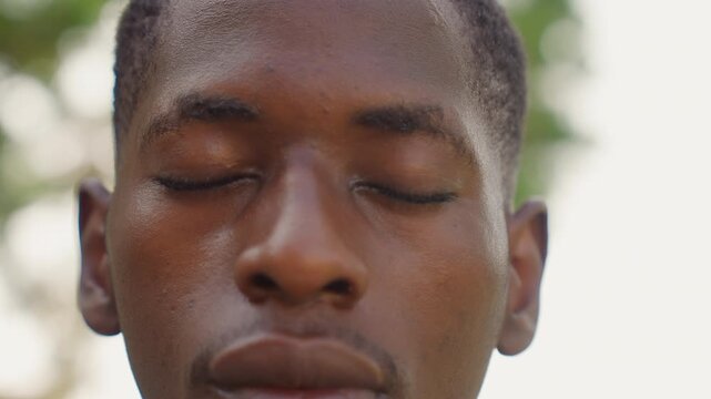 Black sprinter recovering after session, sweat beads on forehead, eyes closed in meditative rest, closeup portrait with soft sunlight and tree bokeh, intimate sport recovery scene