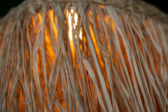 a rustic, textured lampshade made from natural straw or raffia fibers, with a warm light glowing from within that emphasizes the organic, fibrous details.