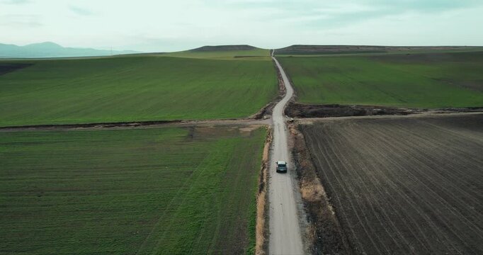 One black suv car driving alone, travel on empty straight asphalt road through agriculture fields at summer sunny day. Aerial drone wide view